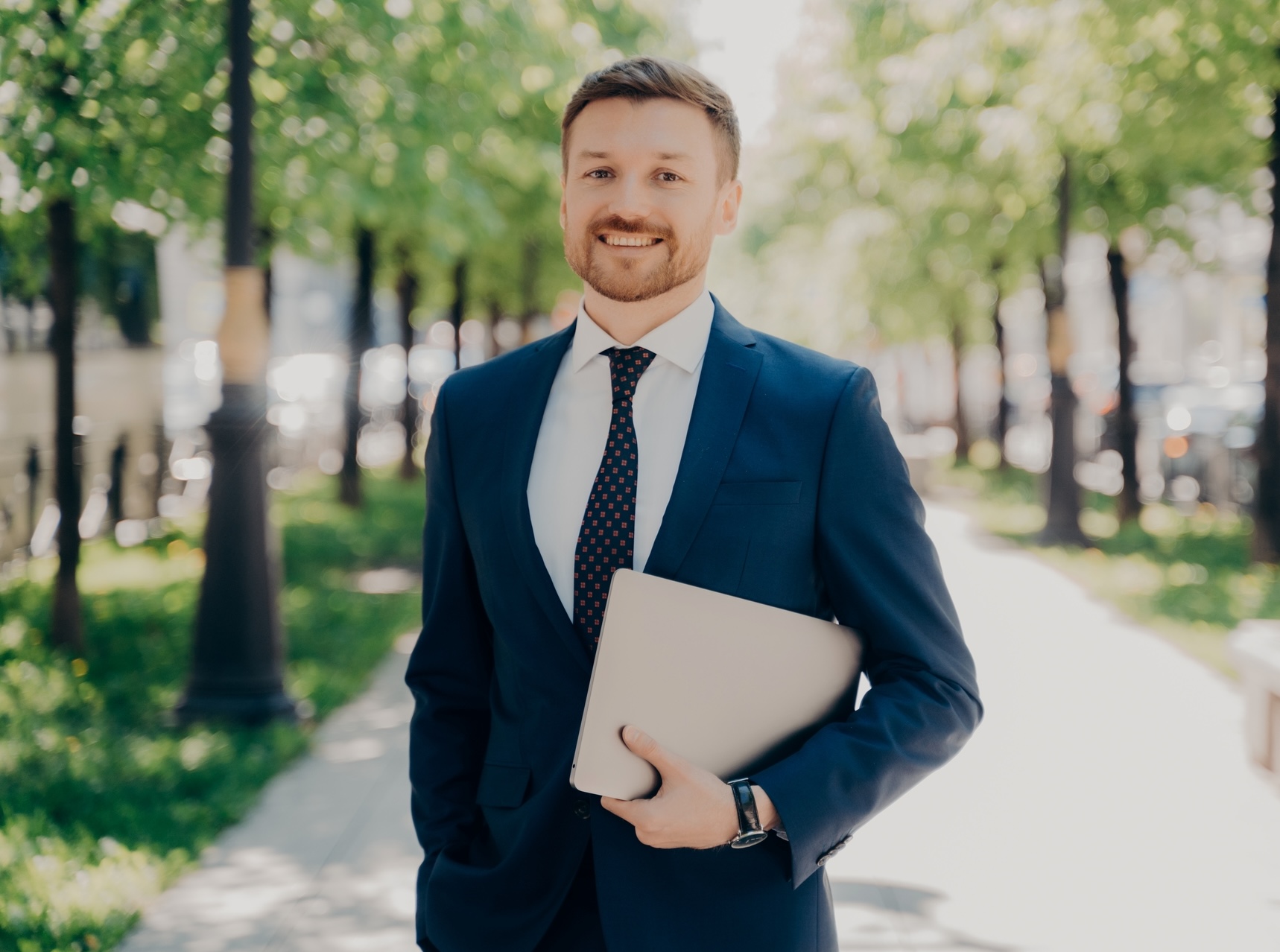 Businessman in suit walking on street holding laptop